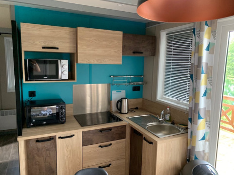 Cocina moderna en Chalet Tribu Premium en Flower Camping La Rivière, Francia, con armarios de madera y pared azul.