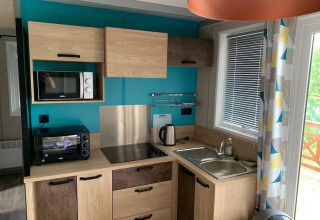 Moderne kitchenette in Chalet Tribu Premium bij Flower Camping La Rivière, Frankrijk, met houten kasten en blauwe muur.