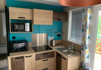 Modern kitchenette in Chalet Tribu Premium at Flower Camping La Rivière, France, with wood cabinets and teal wall.