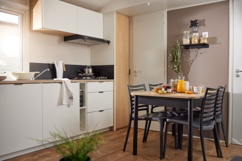 Moderne glampingkeuken en eettafel met vier stoelen, ontbijtgerecht en natuurlijk licht van het raam.