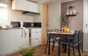 Moderne glamping-køkken og spisebord med fire stole, morgenmad og naturlig belysning fra vinduet.