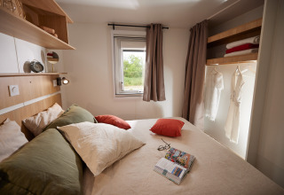 Gezellige glamping slaapkamer met dubbel bed, kussens, open kast en raam met zicht op natuur.