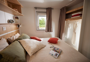Camera da letto glamping con letto matrimoniale, cuscini, armadio aperto e finestra sul verde.