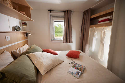 Cozy glamping bedroom featuring a double bed, pillows, open wardrobe, and window with forest view.