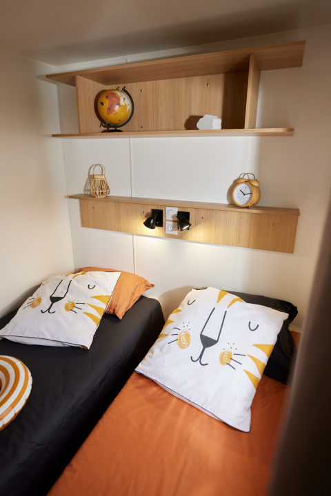 Dos camas individuales con almohadas de león y estanterías de madera en una acogedora habitación glamping.