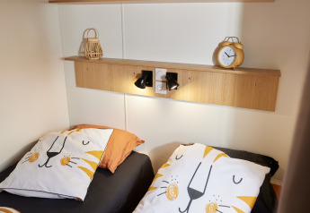 To senge med dyne og pude med løvedesign, træhylder med dekorationer, i et glamping opholdsrum.