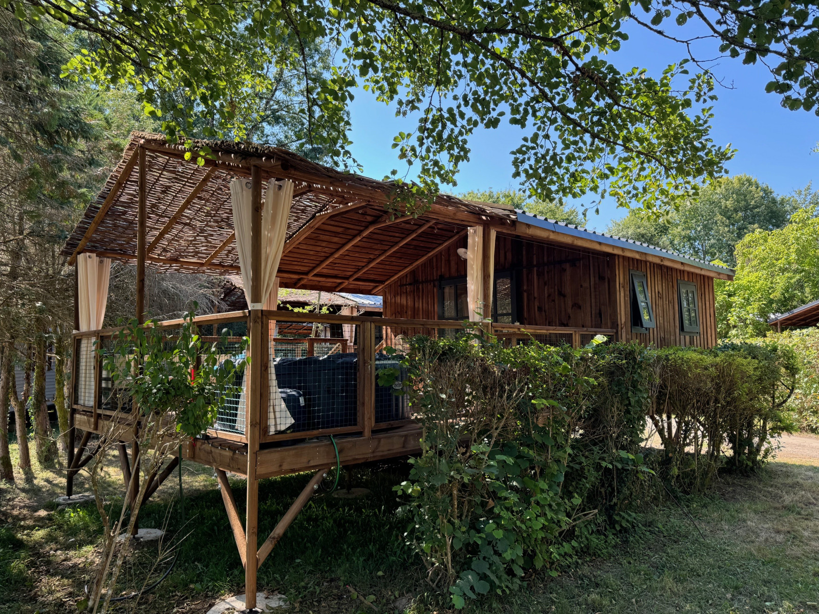 Charme hut met jacuzzi, rustieke houten blokhut met overdekt terras in groene omgeving.