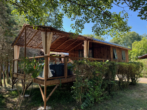 Cabane Charme avec jacuzzi, chalet en bois rustique avec terrasse couverte entourée de verdure.