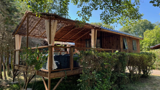Cabane Charme avec jacuzzi, chalet en bois rustique avec terrasse couverte entourée de verdure.