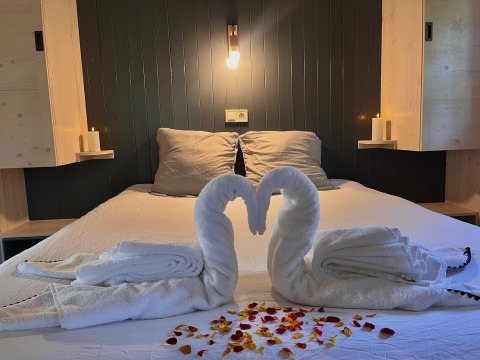 Letto romantico con cigni di asciugamani, candele e petali di rosa nella Charme hut con jacuzzi, Camping Le Périgord.