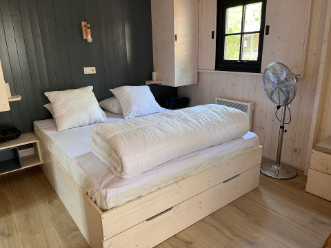 Dormitorio en Charme hut met jacuzzi en Camping Le Périgord, Francia, con cama doble y ventilador.