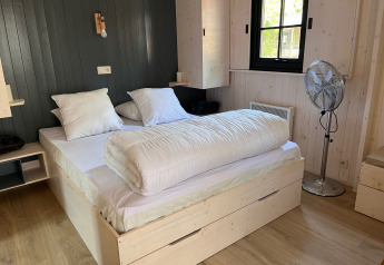 Dormitorio en Charme hut met jacuzzi en Camping Le Périgord, Francia, con cama doble y ventilador.