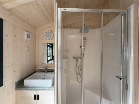Bagno della Charme hut con jacuzzi al Camping Le Périgord, Francia, con doccia e lavandino visibili.
