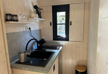 Compact kitchenette in Charme hut with jacuzzi at Camping Le Périgord, featuring a sink and window.