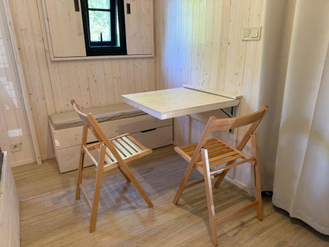 Pequeño comedor con dos sillas plegables de madera y mesa abatible en una acogedora cabaña de madera.