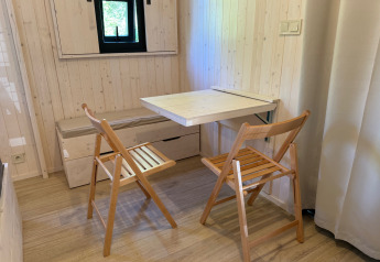 Pequeño comedor con dos sillas plegables de madera y mesa abatible en una acogedora cabaña de madera.