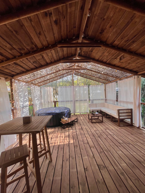 Terrasse en bois couverte avec jacuzzi, coin salon et rideaux au Charme hut met jacuzzi, Camping Le Périgord.