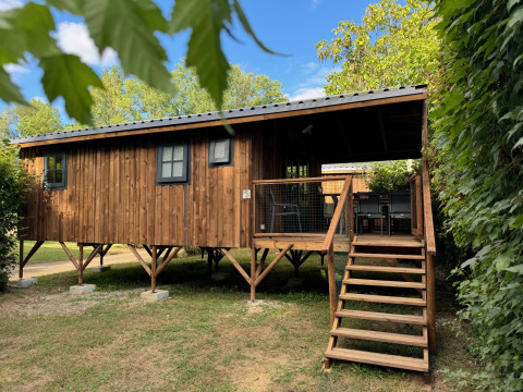 Cabane Premium Hut en bois sur pilotis avec terrasse et escaliers, entourée d’arbres sous ciel bleu.