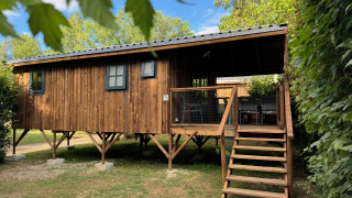 Premium Hut Holzhütte auf Stelzen mit Veranda und Treppe, umgeben von Bäumen und blauem Himmel.