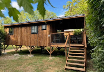 Premium Hut houten blokhut op palen met terras en trap, omringd door bomen en blauwe lucht.