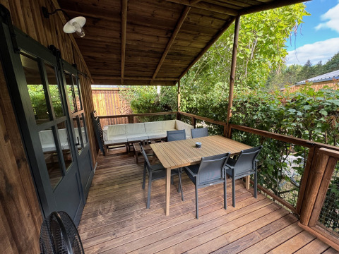 Terrasse en bois couverte à la Premium Hut du Camping Le Périgord, France, aménagée avec table et chaises.