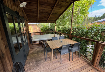 Terrazza in legno coperta alla Premium Hut di Camping Le Périgord, Francia, con tavolo e sedie da esterno.