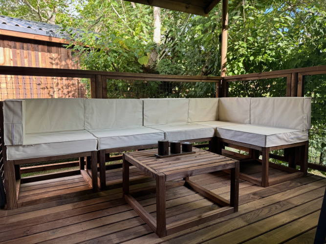 Zona de estar exterior con muebles de madera y cojines blancos en Premium Hut en Camping Le Périgord, Francia.