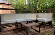 Area salotto esterna con mobili in legno e cuscini bianchi alla Premium Hut, Camping Le Périgord, Francia.