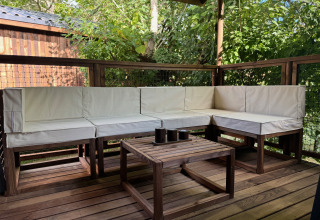 Zona de estar exterior con muebles de madera y cojines blancos en Premium Hut en Camping Le Périgord, Francia.