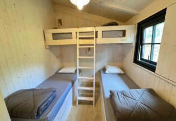 Værelse i Premium Hut, Camping Le Périgord, Frankrig med to enkeltsenge og en køjeseng, lyst træinteriør.