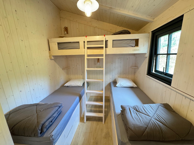 Habitación de Premium Hut en Camping Le Périgord, Francia, con dos camas individuales y una litera, madera clara.
