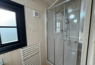 Bagno moderno nella Premium Hut del Camping Le Périgord, Francia, con doccia in vetro e pareti in legno chiaro.