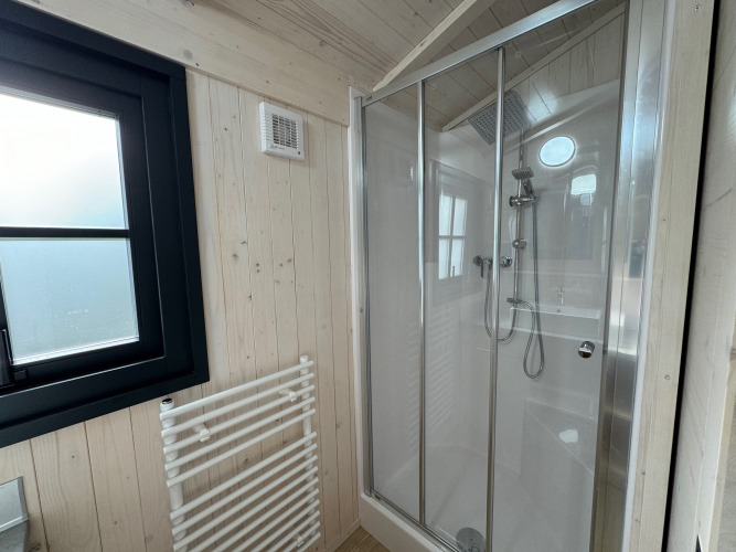 Baño moderno en la Premium Hut del Camping Le Périgord, Francia, con ducha de vidrio y paredes de madera clara.