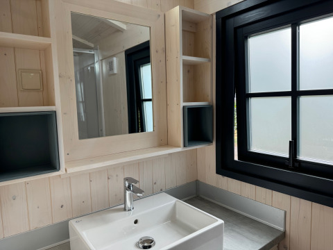 Salle de bain moderne dans la Premium Hut au Camping Le Périgord, France, avec lavabo, miroir et fenêtre noire.