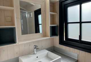 Bagno moderno nella Premium Hut al Camping Le Périgord in Francia, con lavandino, specchio e finestra nera.