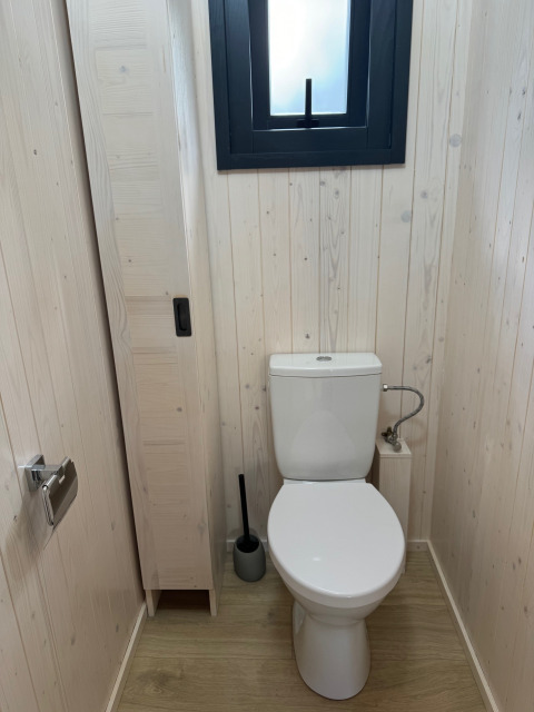 Toilettes modernes dans la Premium Hut du Camping Le Périgord, France, avec murs en bois clair et fenêtre.