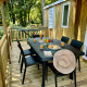 Buiten eethoek op houten terras bij Comfort Cottage, gedekte tafel met fruit, sap en hoed.