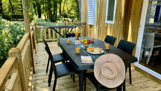 Terraza de madera en Comfort Cottage, mesa preparada con fruta, jugo y sombrero de paja.
