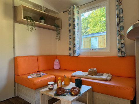 Zona soggiorno accogliente al Comfort Cottage di Camping Le Périgord in Francia con divano arancione e colazione.
