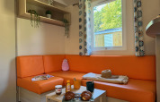 Gezellige zithoek in Comfort Cottage op Camping Le Périgord met oranje sofa en ontbijt op tafel.