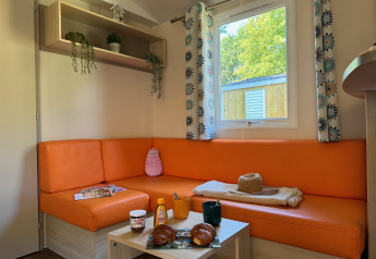 Gezellige zithoek in Comfort Cottage op Camping Le Périgord met oranje sofa en ontbijt op tafel.