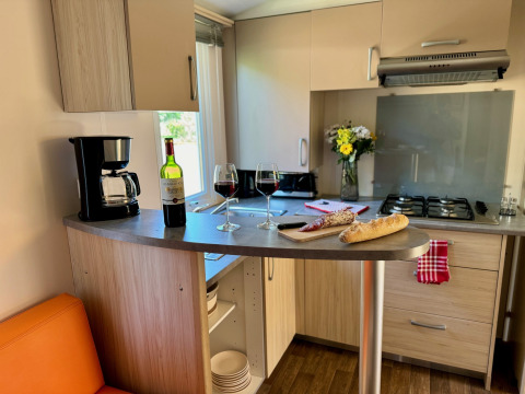 Acogedora cocina en Comfort Cottage de Camping Le Périgord con vino, pan, cafetera y flores frescas.