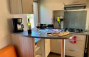 Cucina accogliente al Comfort Cottage di Camping Le Périgord con pane, vino, macchina del caffè e fiori.