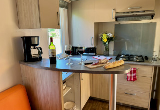 Acogedora cocina en Comfort Cottage de Camping Le Périgord con vino, pan, cafetera y flores frescas.