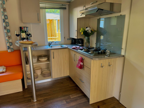 Acogedora cocina en Comfort Cottage, Camping Le Périgord, Francia con vino, pan, flores y vajilla.