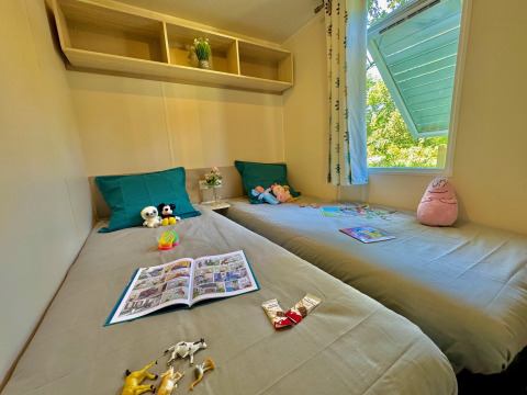 Camera per bambini con due letti singoli, giocattoli e libri al Comfort Cottage del Camping Le Périgord, Francia.