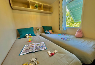 Camera per bambini con due letti singoli, giocattoli e libri al Comfort Cottage del Camping Le Périgord, Francia.