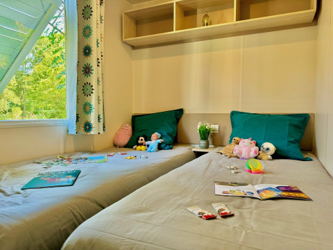 Camera per bambini al Comfort Cottage di Camping Le Périgord, Francia, con giochi, giocattoli e finestra sul verde.