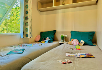 Kids' bedroom in Comfort Cottage at Camping Le Périgord, France, with toys, games, and a window view of nature.
