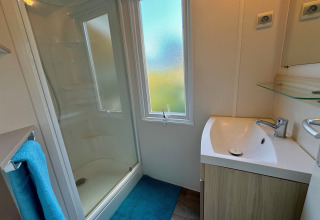 Bagno moderno in Comfort Cottage a Camping Le Périgord, con doccia, lavandino e grande finestra.